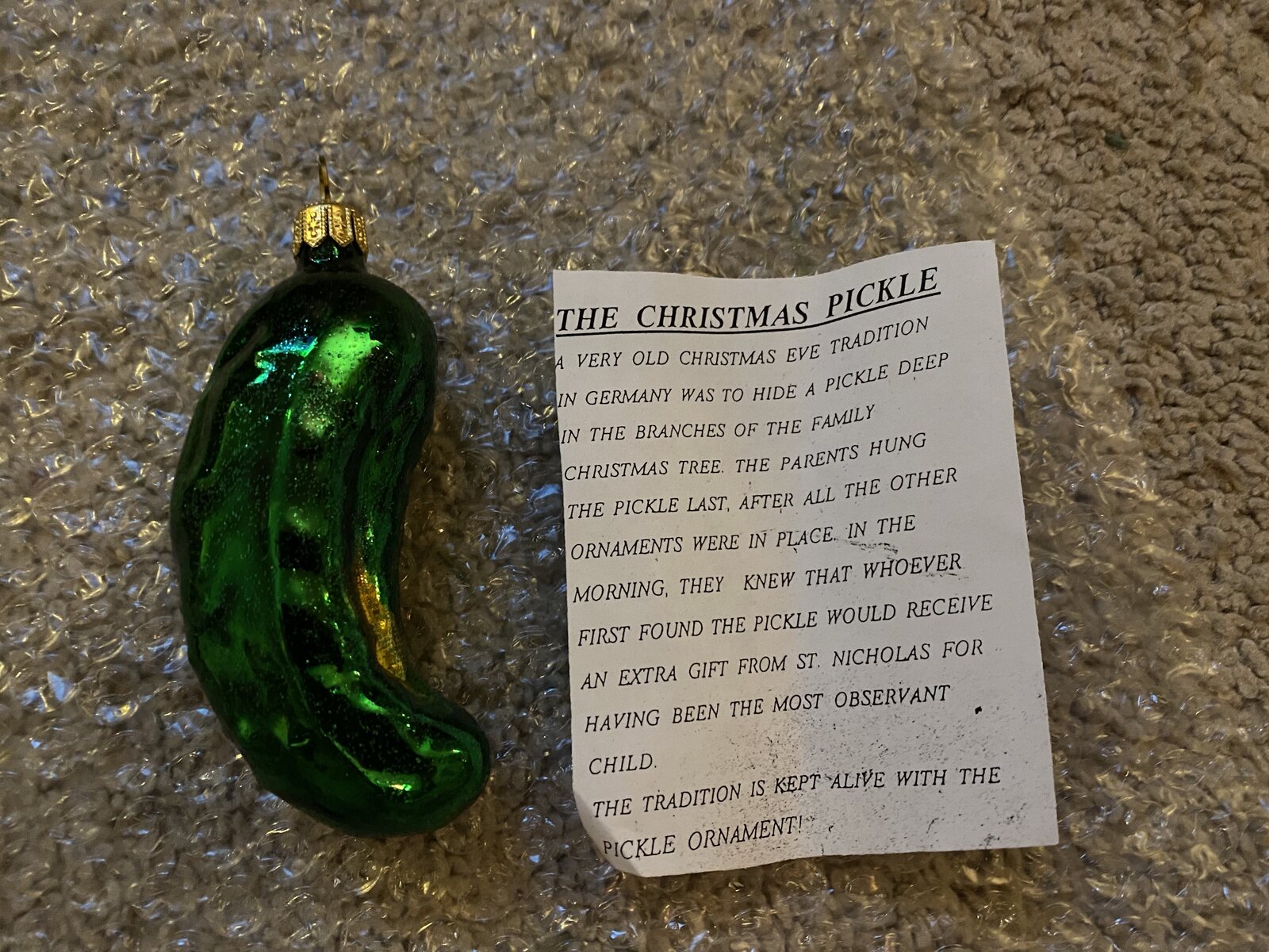 A green glass pickle ornament beside its printed legend card